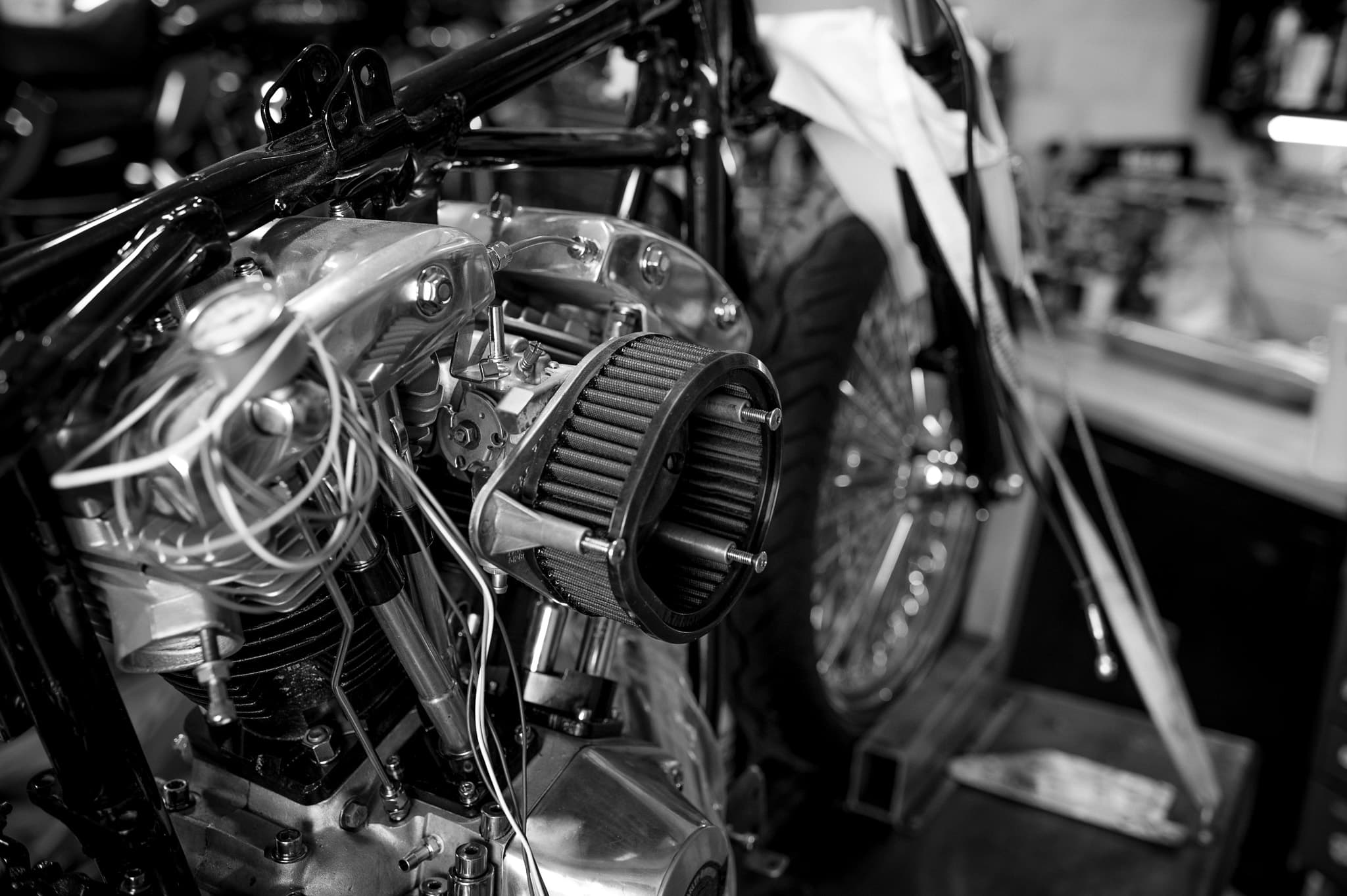 Black-and-white close-up of a chrome air cleaner and engine on a chopper in the shop